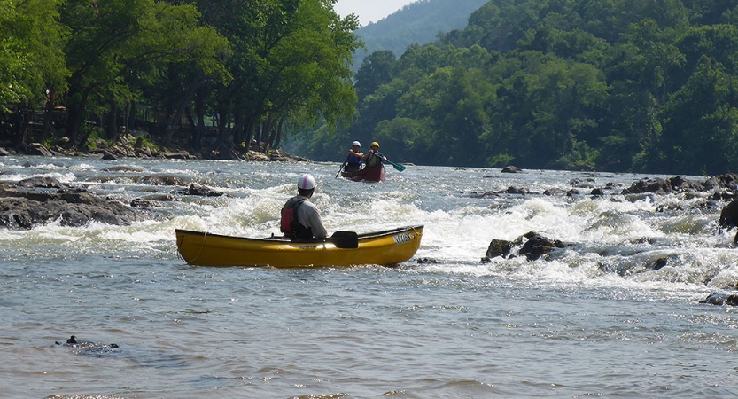 a person in a yellow canoe looks upriver at an oncoming canoe with two people in it 